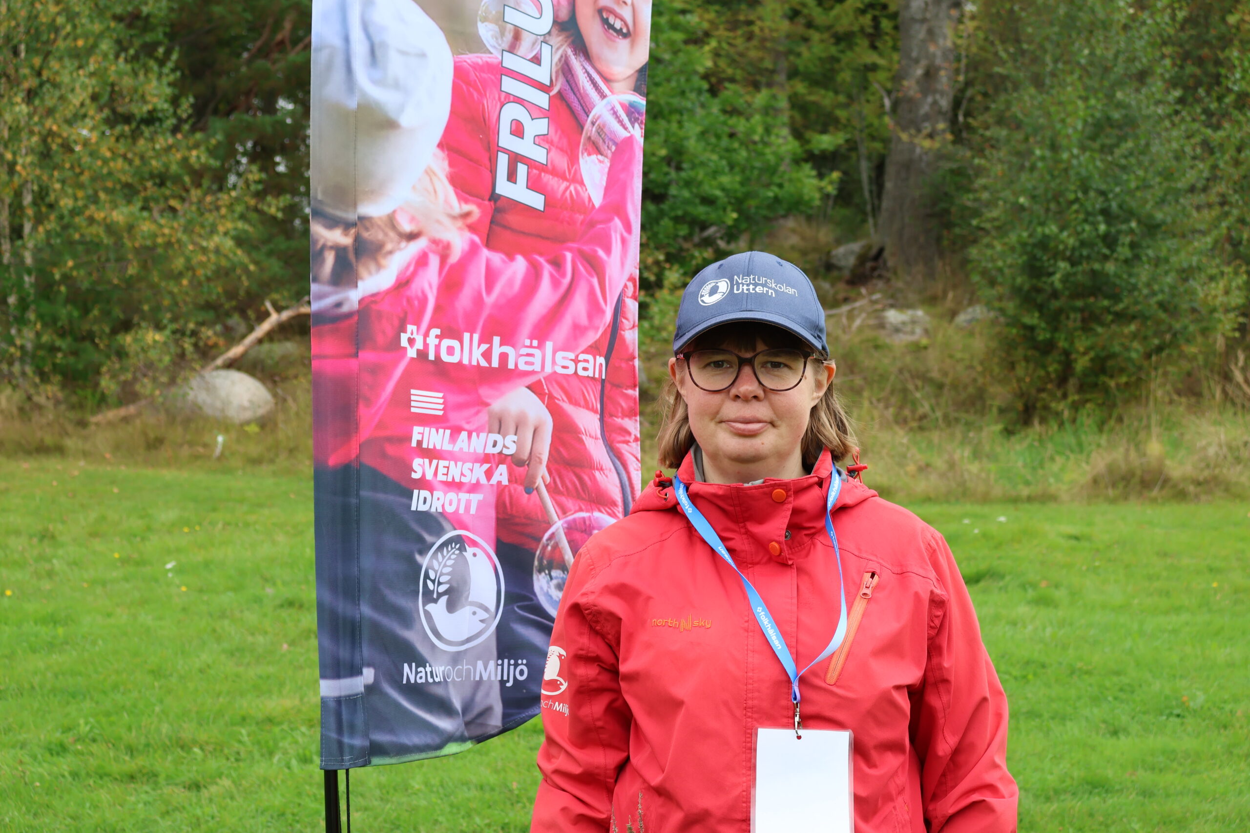 Fotografi på Emilia Nordling framför en Friluftslördag-flagga, utomhus.